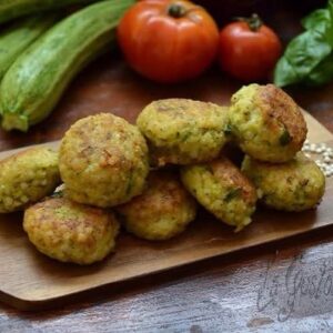Polpette di sorgo e zucchine cotte al forno, dorate e croccanti, servite su tagliere di legno.